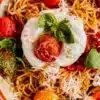 Burrata pasta topped with fresh basil and tomatoes, showcasing creamy cheese.