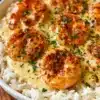 Garlic butter shrimp served over a bed of fluffy rice, garnished with fresh herbs.