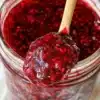 Homemade raspberry jam in a jar with fresh raspberries and toast.