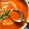 A bowl of homemade tomato basil soup garnished with fresh basil leaves.
