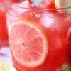 A refreshing glass of watermelon lemonade with vibrant colors and lemon slices on the rim.