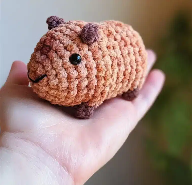 A cute Pocket Capybara sitting comfortably in a person's hand.